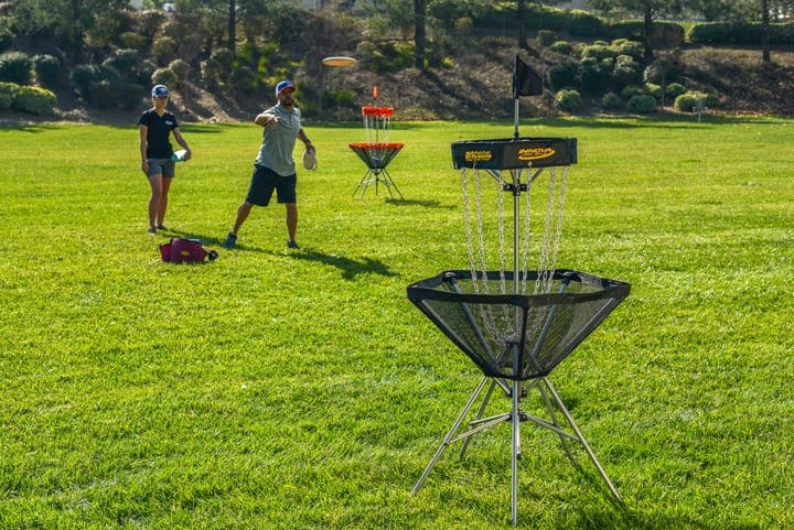 A man and a women putting at a portable disc golf basket