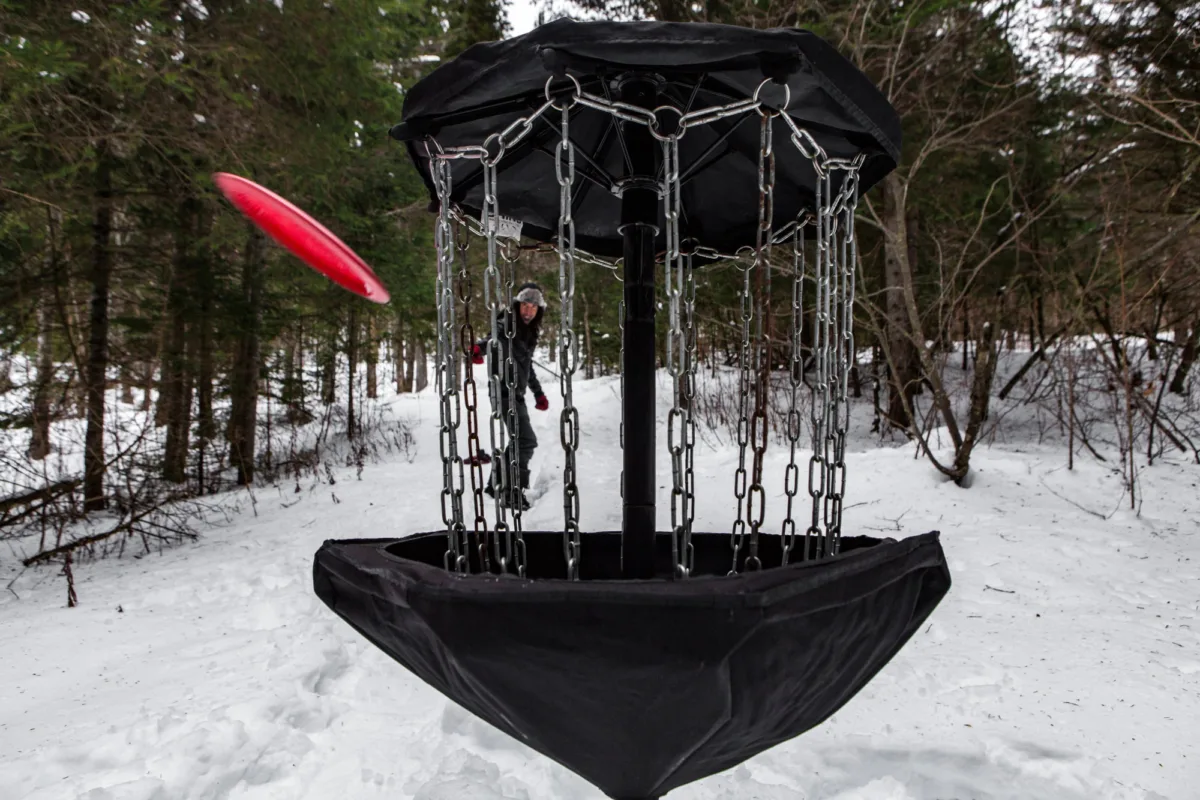 Winter disc golf. Player putting a basket in the snow.