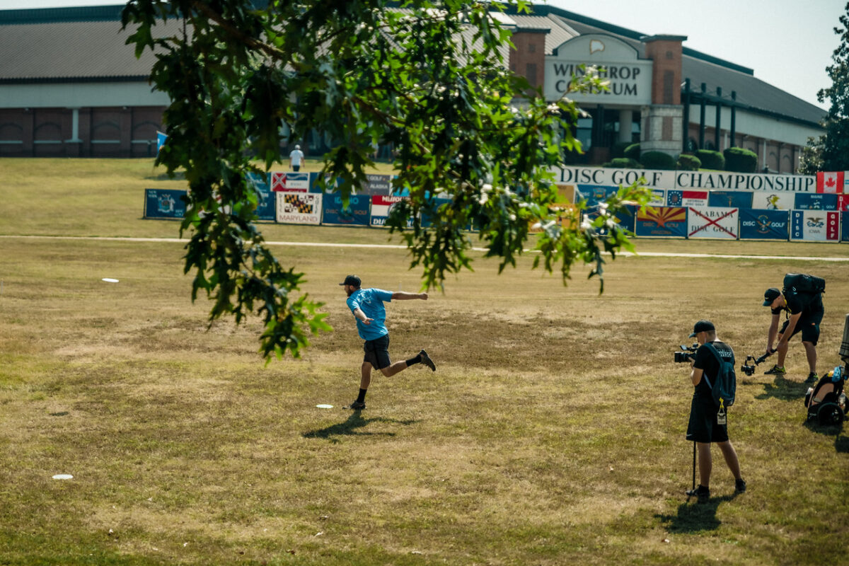 Professional disc golfer properly throwing his drive from behind his lie. 